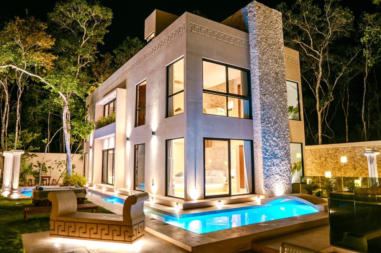 Render nocturno de una residencia de lujo de dos nieles con alberca frente, fachada iluminada y detalles de piedra y grecas decorativas